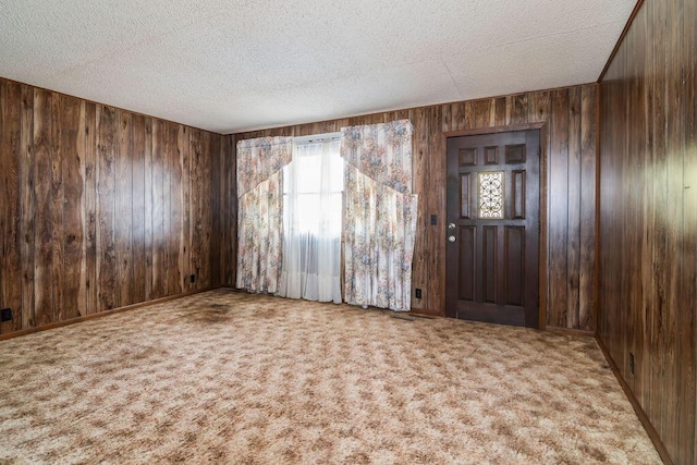 carpeted foyer entrance featuring wood walls and a textured ceiling