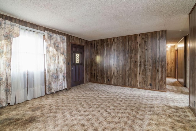 carpeted spare room featuring wooden walls and a textured ceiling