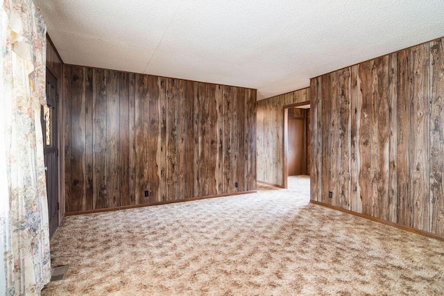 carpeted spare room featuring a textured ceiling and wooden walls