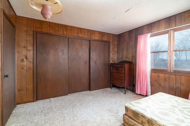 carpeted bedroom featuring a textured ceiling, a closet, and wood walls