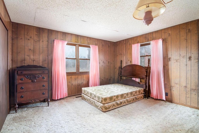 bedroom with a textured ceiling, light colored carpet, and wood walls