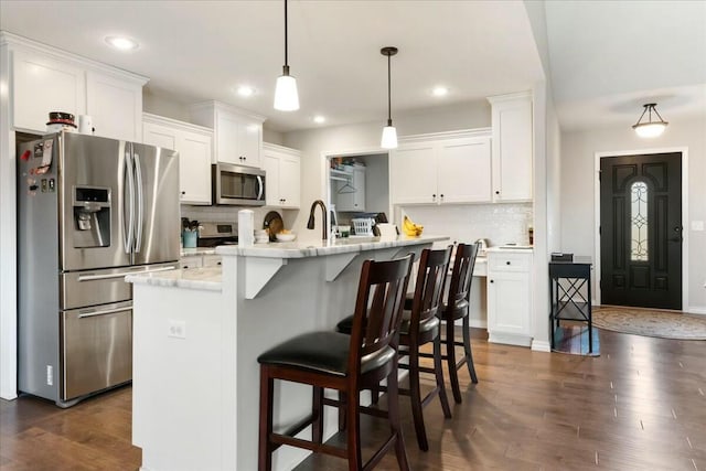 kitchen with a kitchen bar, appliances with stainless steel finishes, white cabinetry, and a center island with sink