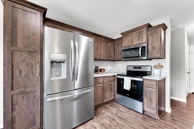 kitchen with light hardwood / wood-style flooring, dark brown cabinetry, light stone countertops, and appliances with stainless steel finishes