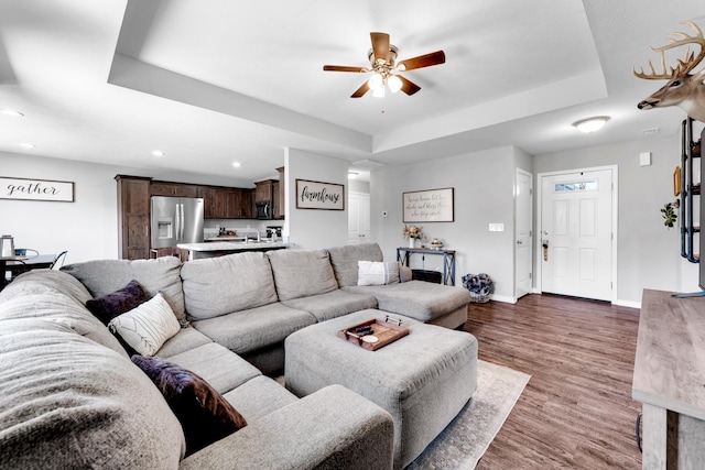 living room featuring dark hardwood / wood-style floors, ceiling fan, and a raised ceiling