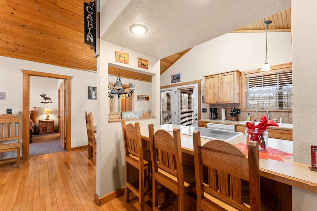 dining space with a textured ceiling, light hardwood / wood-style floors, sink, a notable chandelier, and vaulted ceiling