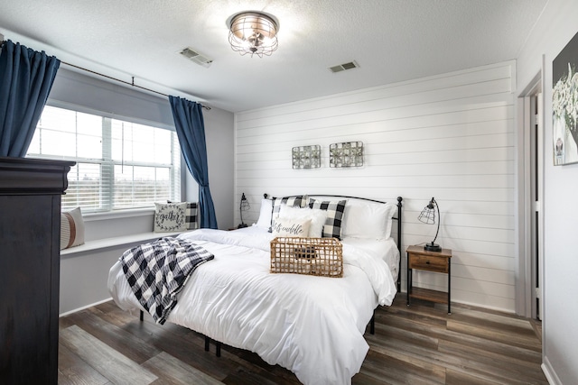 bedroom with dark hardwood / wood-style flooring, wood walls, and a textured ceiling