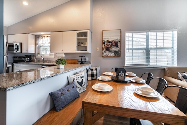 kitchen with appliances with stainless steel finishes, white cabinetry, kitchen peninsula, stone countertops, and lofted ceiling