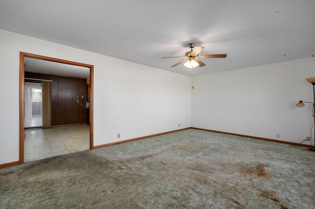 carpeted empty room with wood walls and ceiling fan