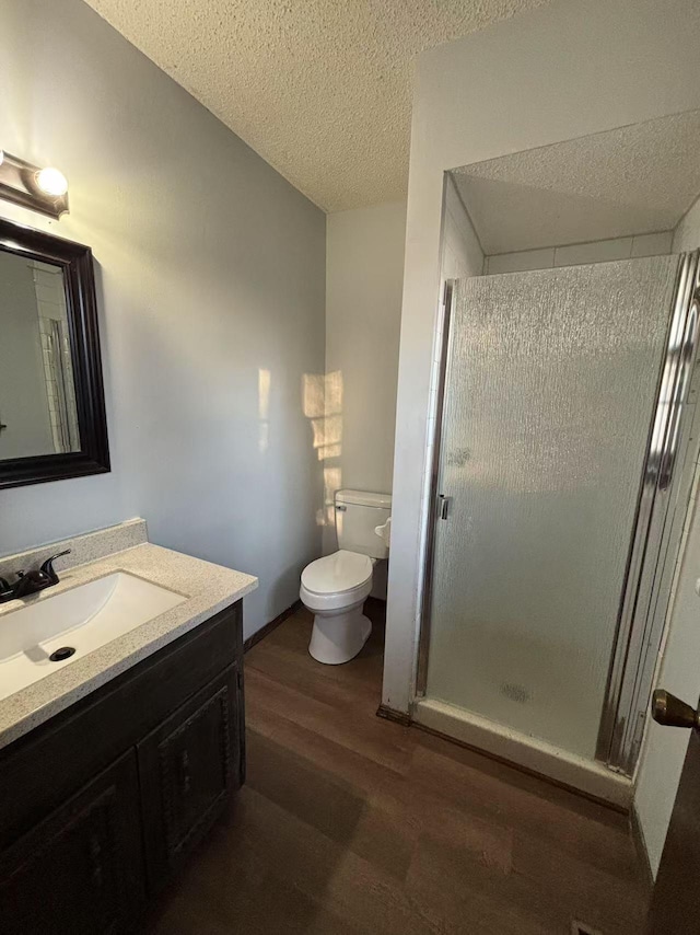 bathroom with wood-type flooring, toilet, a textured ceiling, a shower with shower door, and vanity