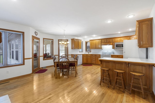 kitchen with kitchen peninsula, light hardwood / wood-style flooring, hanging light fixtures, white appliances, and a notable chandelier