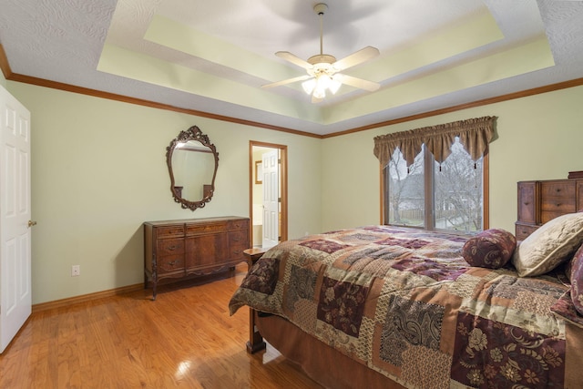 bedroom featuring light wood-type flooring, ceiling fan, crown molding, and a tray ceiling