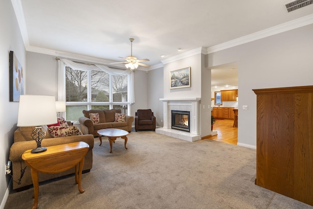 living room with ceiling fan, light colored carpet, a tile fireplace, and ornamental molding