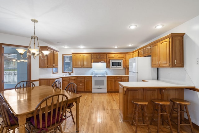 kitchen with white appliances, sink, hanging light fixtures, kitchen peninsula, and light hardwood / wood-style flooring