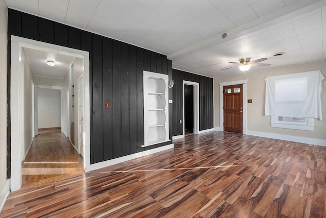 spare room with built in shelves, ceiling fan, hardwood / wood-style floors, and wood walls