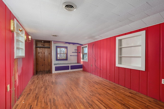 empty room featuring built in features, wooden walls, and wood-type flooring