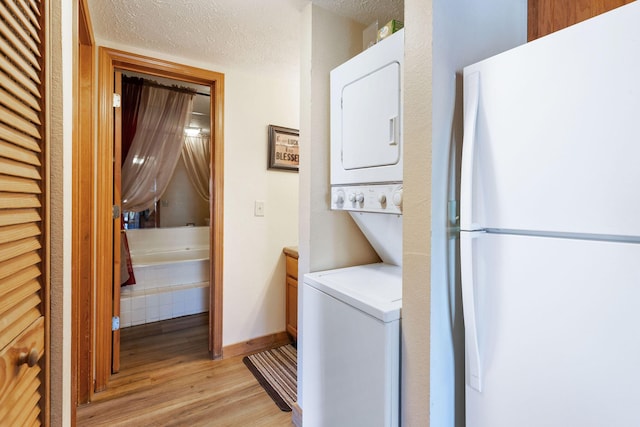 washroom with stacked washer / dryer, light hardwood / wood-style floors, and a textured ceiling