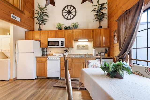 kitchen featuring light hardwood / wood-style floors, a towering ceiling, white appliances, and stacked washer / dryer