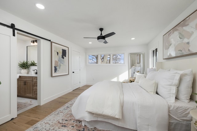 bedroom with ceiling fan, light hardwood / wood-style floors, ensuite bathroom, and a barn door