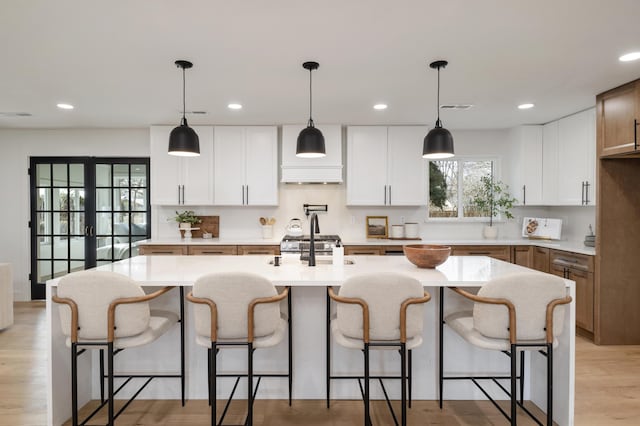 kitchen with white cabinets, stainless steel range oven, a kitchen island with sink, and pendant lighting