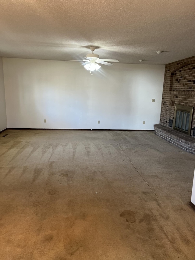 unfurnished living room featuring ceiling fan, a brick fireplace, a textured ceiling, and carpet flooring