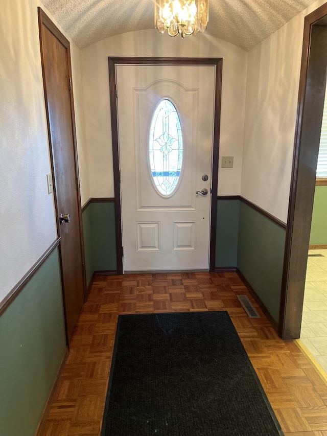 foyer with dark parquet flooring, lofted ceiling, and an inviting chandelier