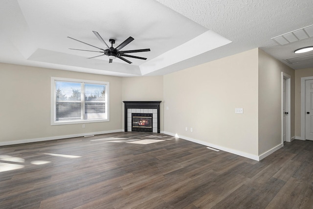 unfurnished living room featuring a tile fireplace, dark wood-type flooring, a textured ceiling, and a tray ceiling