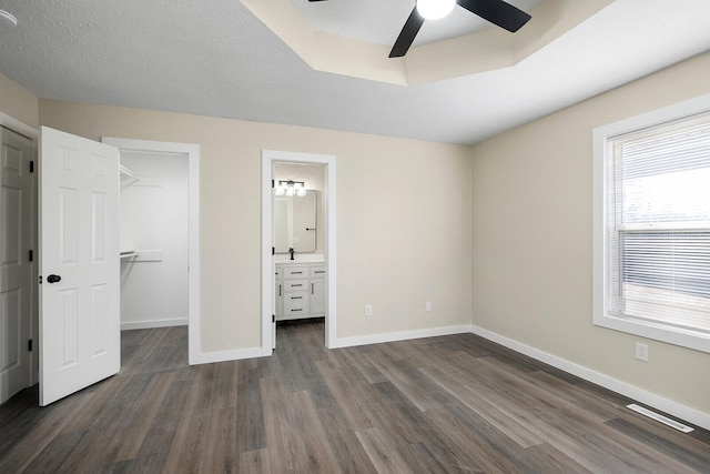 unfurnished bedroom featuring ensuite bath, a walk in closet, a closet, ceiling fan, and dark hardwood / wood-style floors