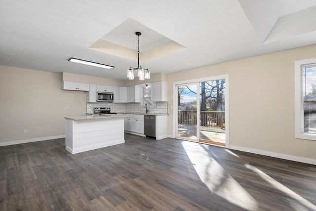 kitchen with appliances with stainless steel finishes, white cabinets, dark wood-type flooring, pendant lighting, and a tray ceiling