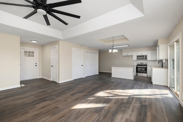 unfurnished living room with sink, ceiling fan with notable chandelier, dark hardwood / wood-style flooring, and a tray ceiling