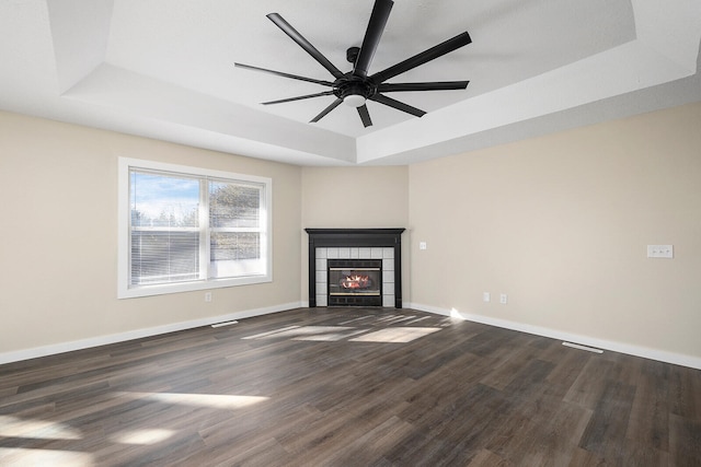 unfurnished living room featuring ceiling fan, dark hardwood / wood-style floors, a raised ceiling, and a tiled fireplace