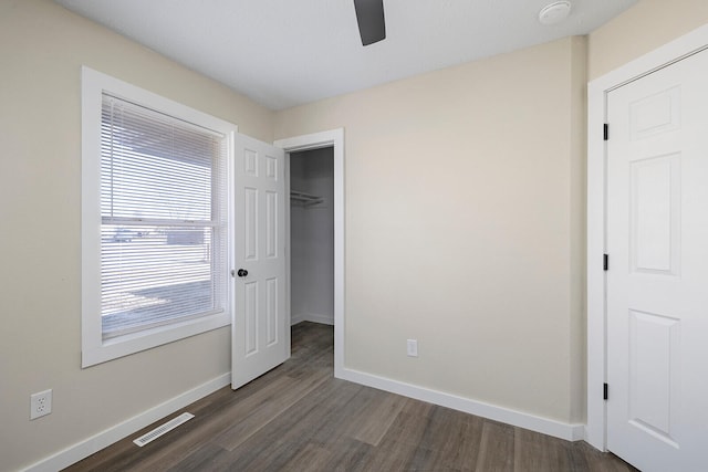 unfurnished bedroom featuring a closet, a walk in closet, ceiling fan, and dark hardwood / wood-style flooring