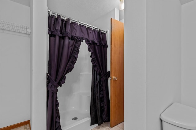 bathroom featuring a shower with curtain, toilet, and a textured ceiling