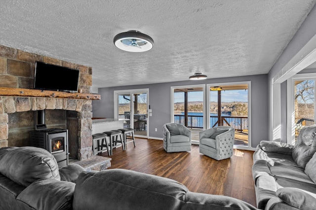 living room featuring a wood stove, a textured ceiling, dark hardwood / wood-style flooring, and a water view