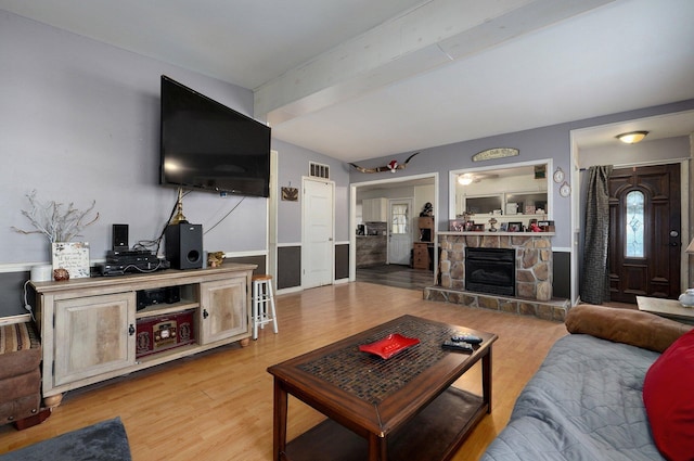 living room featuring a stone fireplace, beamed ceiling, and light hardwood / wood-style floors