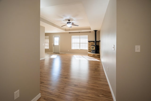 unfurnished living room featuring hardwood / wood-style floors, a raised ceiling, ceiling fan, and a wood stove