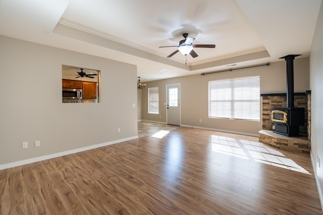 unfurnished living room with crown molding, a tray ceiling, light wood-type flooring, and a wood stove