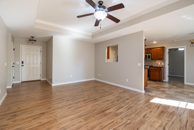 unfurnished living room featuring ornamental molding, light hardwood / wood-style flooring, ceiling fan, and a tray ceiling