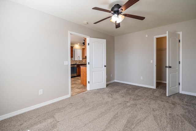 unfurnished bedroom featuring a walk in closet, sink, light carpet, and ceiling fan