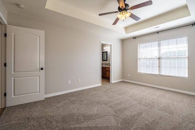 unfurnished bedroom featuring ceiling fan, connected bathroom, a raised ceiling, and carpet