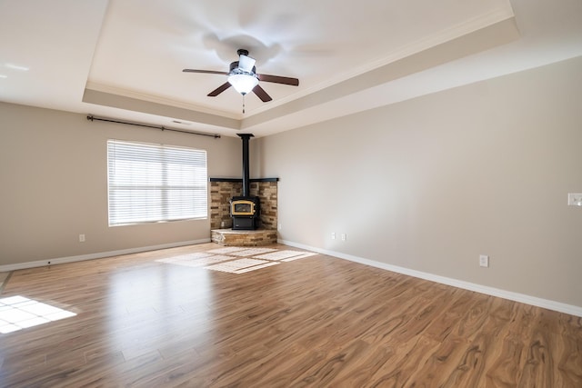 unfurnished living room featuring a tray ceiling, light wood-type flooring, ceiling fan, and a wood stove