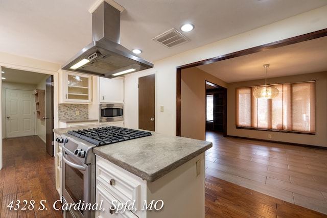 kitchen with hanging light fixtures, appliances with stainless steel finishes, white cabinets, tasteful backsplash, and island range hood