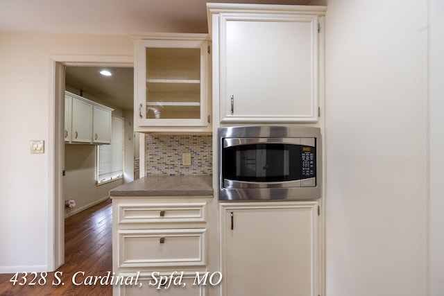 kitchen featuring white cabinetry, stainless steel microwave, dark hardwood / wood-style flooring, and tasteful backsplash