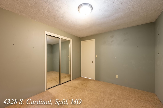 unfurnished bedroom featuring a textured ceiling, a closet, and light carpet