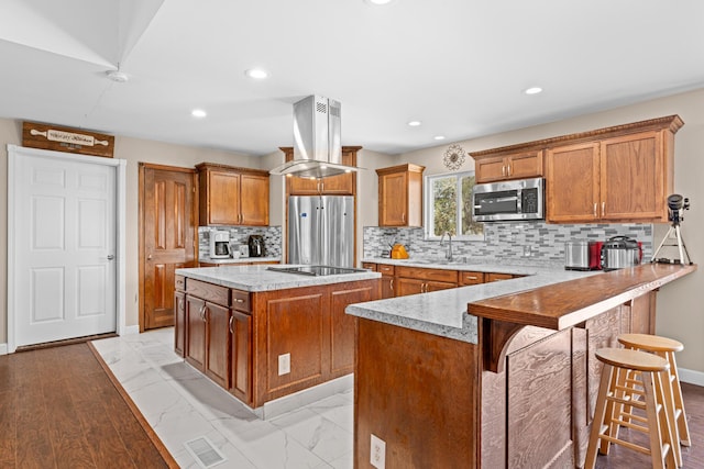 kitchen featuring a kitchen breakfast bar, kitchen peninsula, island exhaust hood, a kitchen island, and stainless steel appliances