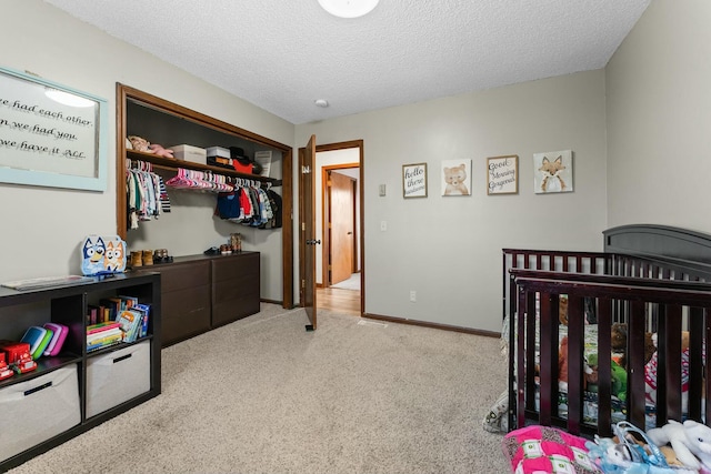 carpeted bedroom featuring a textured ceiling, a nursery area, and a closet