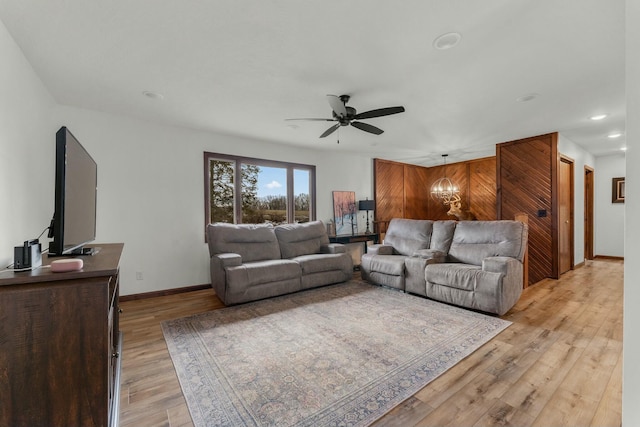 living room featuring ceiling fan with notable chandelier and light hardwood / wood-style flooring