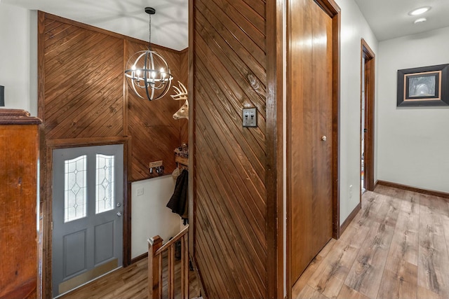 entrance foyer featuring light wood-type flooring, wooden walls, and an inviting chandelier