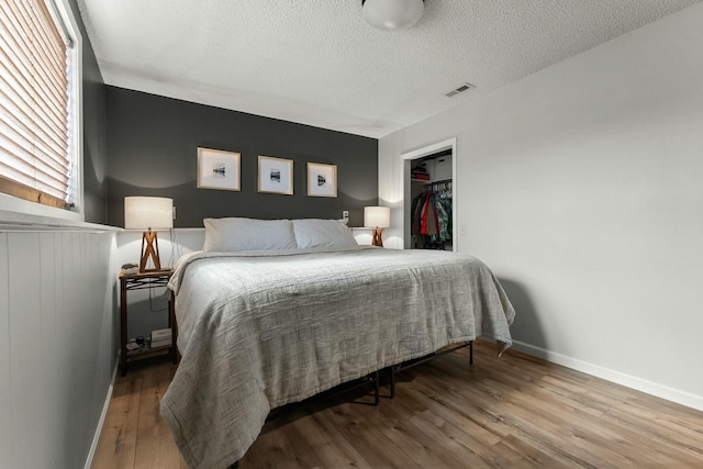 bedroom with hardwood / wood-style flooring, a textured ceiling, a closet, and a walk in closet