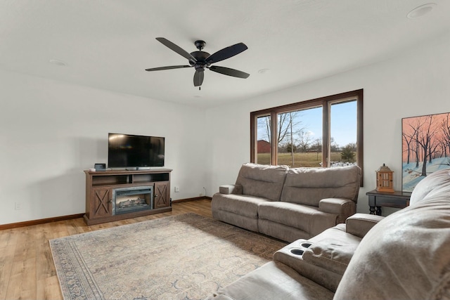 living room with a fireplace, ceiling fan, and light wood-type flooring