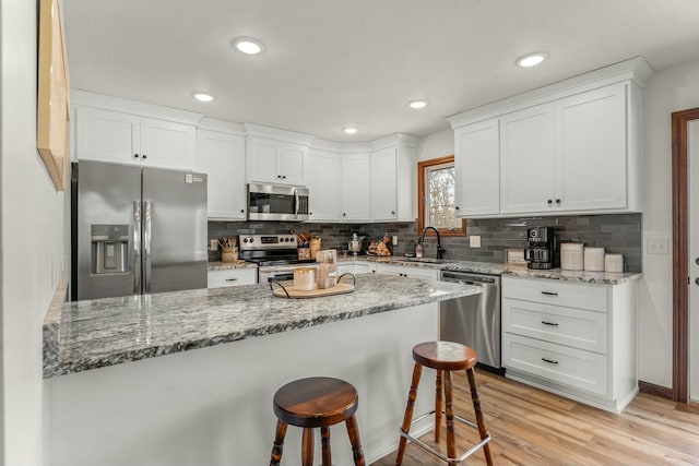 kitchen with light stone counters, white cabinets, a breakfast bar area, and stainless steel appliances